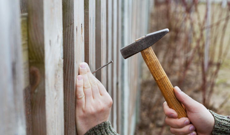 man hands drive nail with a hammer in wooden fence, carpentry